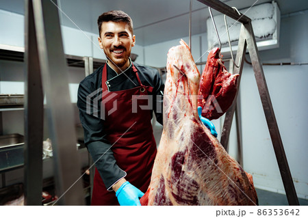 Male butcher standing by meat hanging on hook in meat shop 86353642