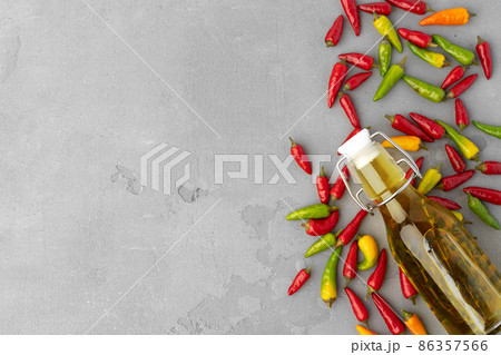 Bottle of olive oil and chili peppers on gray background Bottle of olive oil and chili peppers on gray background 86357566