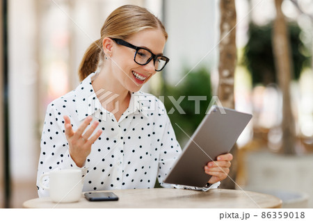 Positive woman tutor waving hello at webcam on digital tablet while giving online lesson outside Positive woman tutor waving hello at webcam on digital tablet while giving online lesson outside 86359018