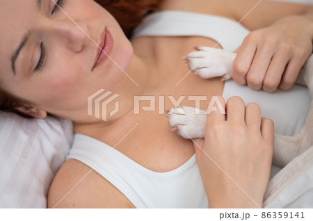 Caucasian woman lies on her back and holds a dog by the paws.  86359141