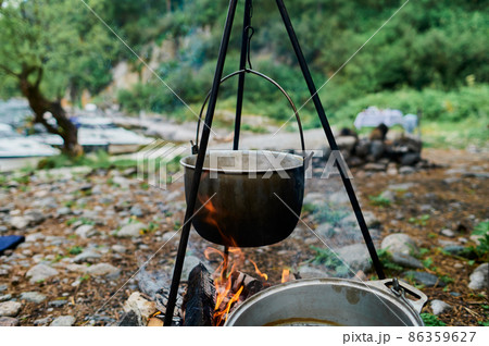 Bowler cooking food bonfire cauldron camp fire, pot. Hiking pot in the bonfire. Traveling in the mountains with tents. 86359627