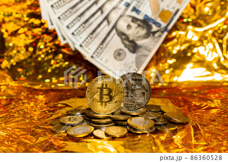Two bitcoins on a stack of coins against a background of hundred-dollar bills arranged in a fan on a golden background. Two bitcoins on a stack of coins against a background of hundred-dollar bills arranged in a fan on a golden background. 86360528