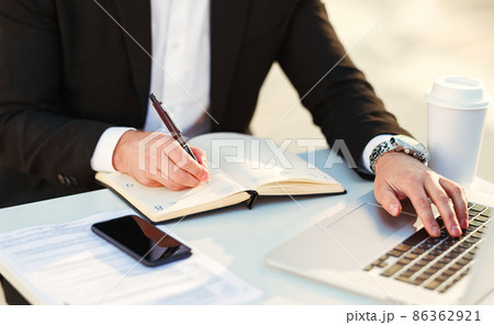 Cropped shot of businessman in suit working remotely on laptop computer at outdoors cafe 86362921