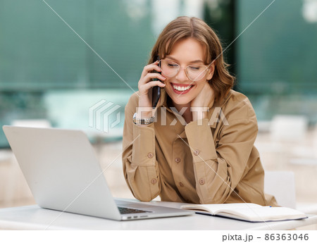 Happy young office assistant working remotely online sitting with laptop and coffee outside Happy young office assistant working remotely online sitting with laptop and coffee outside 86363046