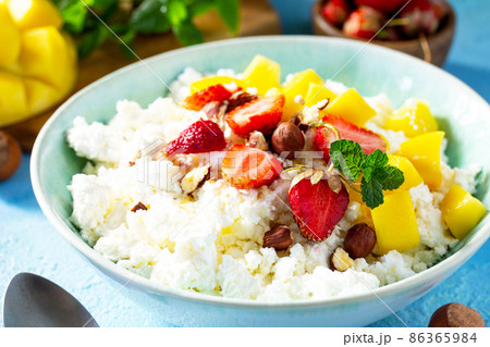 Dietary breakfast for summer time. Fresh cottage cheese close-up with strawberry, mango and nuts on a light blue stone or slate table. Dietary breakfast for summer time. Fresh cottage cheese close-up with strawberry, mango and nuts on a light blue stone or slate table. 86365984