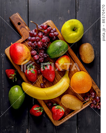 Juicy ripe fruits. Strawberry, kiwi, apple, pear, banana, avocado, grape. Assorted delicious tropical fruits on a wooden background. Vertical shot 86370470