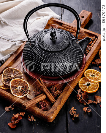 Cast iron black teapot. Cinnamon sticks, star anise, dry orange slices and dried ginger on a cutting board. Still life. Copy space. Vertical shot Cast iron black teapot. Cinnamon sticks, star anise, dry orange slices and dried ginger on a cutting board. Still life. Copy space. Vertical shot 86370472