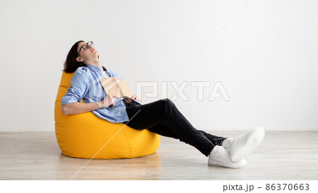 Remote education concept. Bored male student sleeping with book, sitting in beanbag chair, panorama, free space 86370663