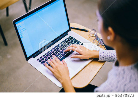 Unrecognizable female sitting at table and typing on laptop Unrecognizable female sitting at table and typing on laptop 86370872