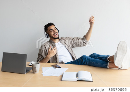 Smiling Arab man leaning back playing virtual guitar Smiling Arab man leaning back playing virtual guitar 86370896