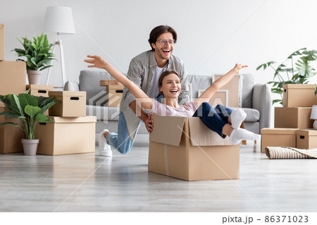Cheerful caucasian man feel playful with happy wife riding in cardboard boxes on moving day to new home 86371023