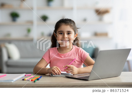 Cute Little Girl Sitting At Table With Laptop And Drawing In Notepad 86371524