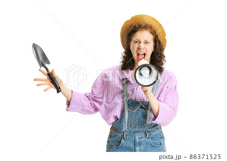 Young beautiful gardener in work uniform and hat shouting at megaphone isolated on white background. Concept of job, emotions, agronomy, eco 86371525