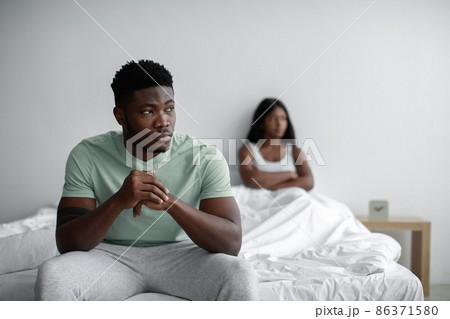 Depressed sad young black man ignores offended lady after quarrel sits on bed in bedroom interior, copy space 86371580