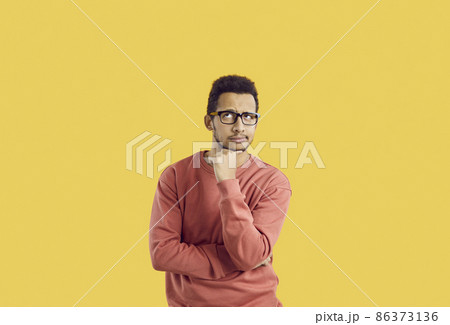 Hmm. Young student in glasses doubting something. Puzzled adult man in casual sweatshirt isolated on solid yellow background looking up and thinking hard about difficult question or future career plan 86373136