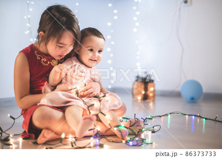 Little sisters having fun at home with chrismass lights. 86373733