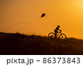 Silhouette of a child riding a bicycle with a kite in his hand 86373843