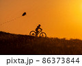 Silhouette of a child riding a bicycle with a kite in his hand 86373844
