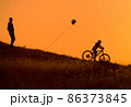 Silhouette of a father and his child riding a bicycle with a kite in his hand 86373845