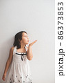 Cute girl standing next to an white wall and blowing kisses 86373853