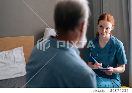 Close-up view from back of senior male patient talking with professional female doctor writing down diagnosis and symptoms in medical history on clipboard at nursing home, selective focus. Close-up view from back of senior male patient talking with professional female doctor writing down diagnosis and symptoms in medical history on clipboard at nursing home, selective focus. 86374232