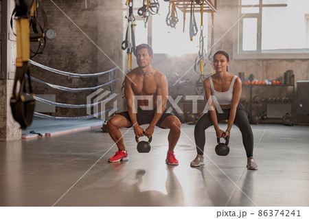Male personal trainer training female client in gym 86374241
