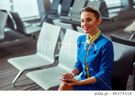 Joyful woman stewardess sitting on chair in airport departure lounge 86374318