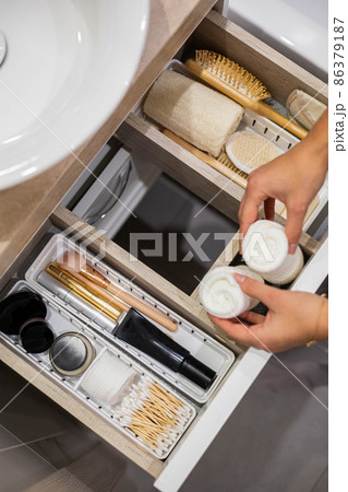 Top view of woman hands neatly organizing bathroom amenities and toiletries in drawer in bathroom. Top view of woman hands neatly organizing bathroom amenities and toiletries in drawer in bathroom. 86379187