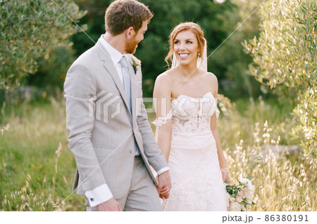 Groom and bride walk among the trees in the park Groom and bride walk among the trees in the park 86380191