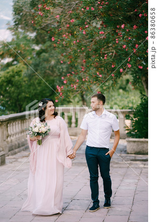 Bride in a pink dress with a bouquet holds the groom hand Bride in a pink dress with a bouquet holds the groom hand 86380658
