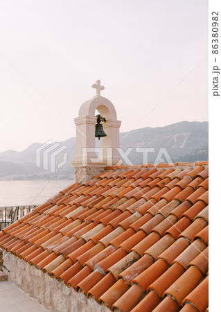 Bell on an old stone bell tower with a red tiled roof 86380982