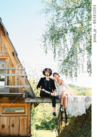 Bride and groom sit on a bridge near a house Bride and groom sit on a bridge near a house 86381003