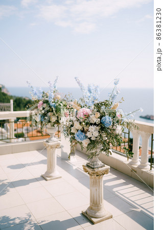 Bouquets of flowers stand on a terrace overlooking the sea 86381230