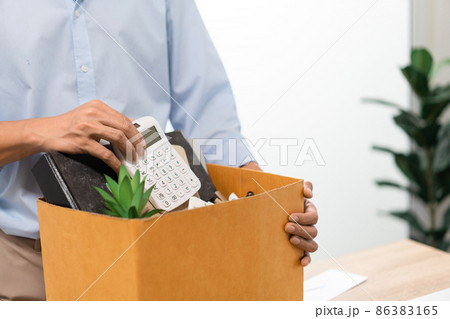 Resignation Concept The man in light blue shirt standing at the desk and putting the calculator and other stuff into the box Resignation Concept The man in light blue shirt standing at the desk and putting the calculator and other stuff into the box 86383165