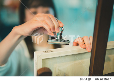 目玉クリップでB3パネルに画用紙を止めてデッサンをする女性の手元 86384087
