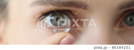 Soft contact lens on female finger against background of female eyes 86384201
