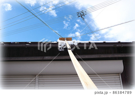 【HDR風】長い棒の先端にブレードを取り付けた自家製の雪搔き道具で屋根に積もった雪を下ろしている場面 86384789