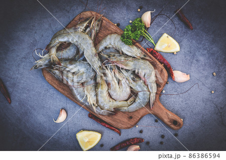 raw shrimps on wooden cutting board plate, fresh shrimp prawns for cooking with spices lemon garlic black pepper chili on dark background in the seafood restaurant, top view 86386594