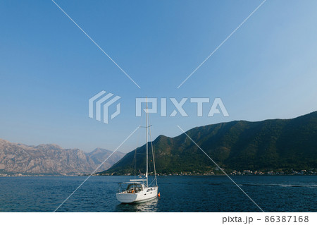 White sailing yacht stands off the coast of Perast against the backdrop of the bay 86387168