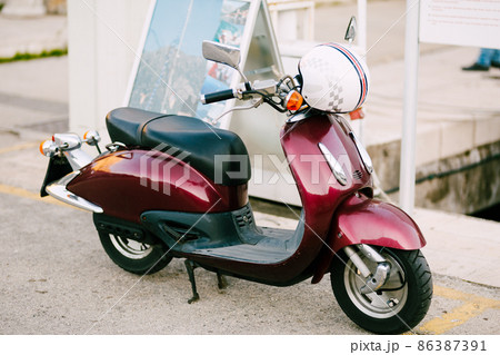 Burgundy motor scooter with a white helmet stands on the street Burgundy motor scooter with a white helmet stands on the street 86387391
