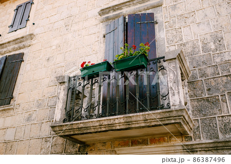 Stone balcony with a wrought iron lattice with flowerpots on the stone facade of the house Stone balcony with a wrought iron lattice with flowerpots on the stone facade of the house 86387496