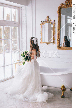 Beautiful bride with bouquet in wedding dress sitting in studio. Bride view from the back Beautiful bride with bouquet in wedding dress sitting in studio. Bride view from the back 86388621