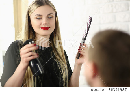 Hairdresser holding comb and spray with water in front of male client in beauty salon Hairdresser holding comb and spray with water in front of male client in beauty salon 86391987