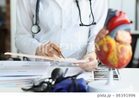 Doctor cardiologist examining cardiogram against background of artificial heart model closeup 86391996