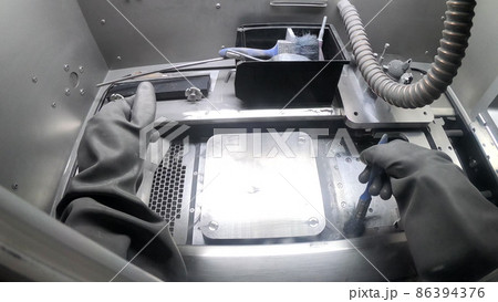Male worker in rubber glove cleans printing platform inside 3d printer for metal 86394376