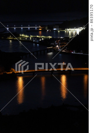 夜明け前に夜景の中の川にかかる鉄橋を進む一両編成のJR日南線キハ40 86395170