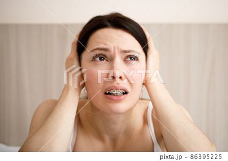 The woman covers her ears because of the loud noise. Noisy neighbors listen to loud music and interfere with sleep. Using earplugs. 86395225