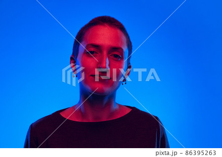 Young calm woman, student with short hair in black sweater looking at camera isolated on dark blue background in neon light. Concept of emotions 86395263