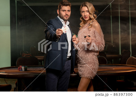 Confident man showing pair of aces while standing with woman in casino Confident man showing pair of aces while standing with woman in casino 86397300
