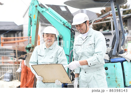 工事現場の重機の前で打ち合わせをする作業員の男性達 工事現場の重機の前で打ち合わせをする作業員の男性達 86398143